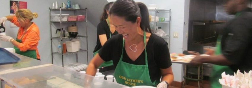 A soup kitchen volunteer happily serving meals to the guests.
