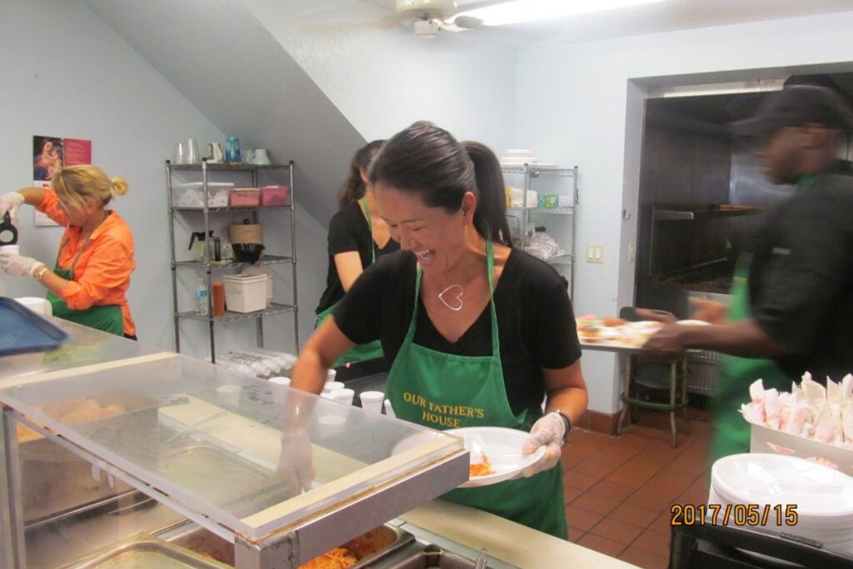 A soup kitchen volunteer happily serving meals to the guests.