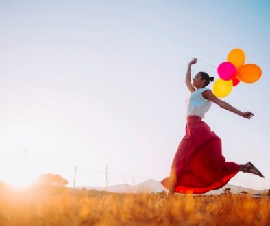 A woman carrying balloons while running into the sunrise, a picture of happiness.