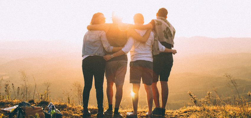 A group of friends facing the sunrise hand in hand.