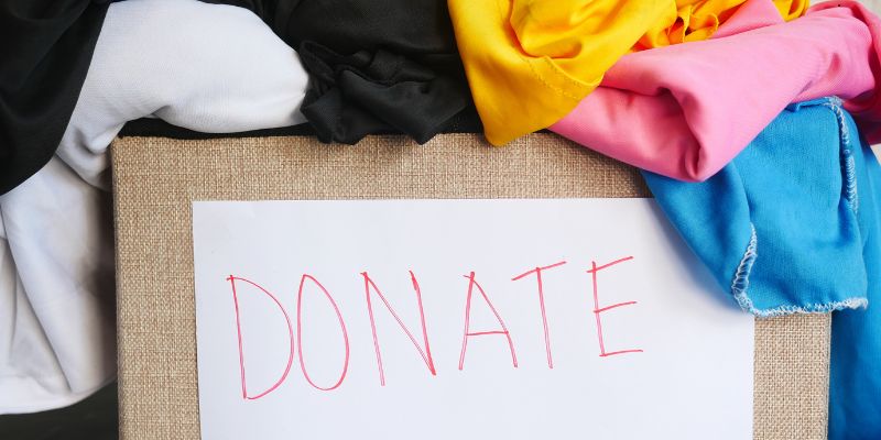 Cardboard donation box overflowing with colorful clothing and scrap fabric ready to donate scrap fabric to charity or crafting programs.