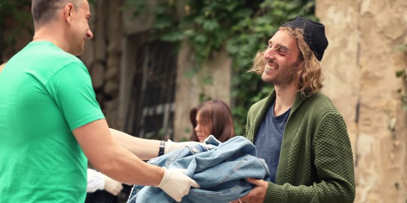 A homeless person is happy to receive old clothes from one of the charity volunteers.