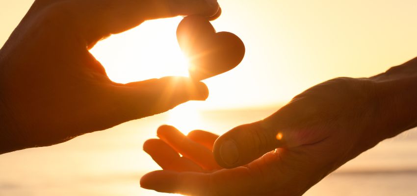 Two hands forming a heart shape with a glowing sunset, symbolizing kindness in the bible and God's love.