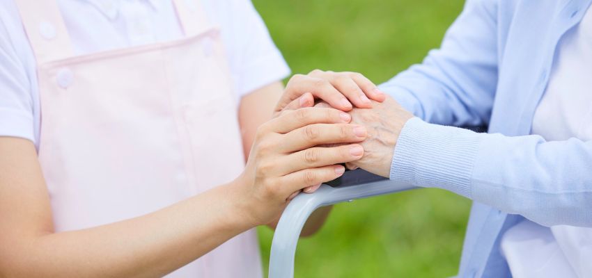 A young caregiver gently holding an elderly woman's hand on a walker in a garden, representing compassion and kindness in the bible.